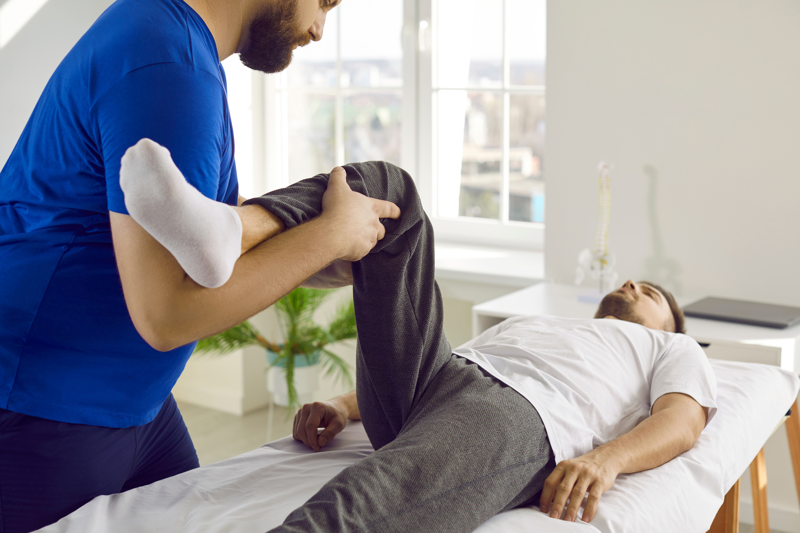 Chiropractor, Osteopath or Physiotherapist Treating Patient's Pain and Examining Knee Flexion